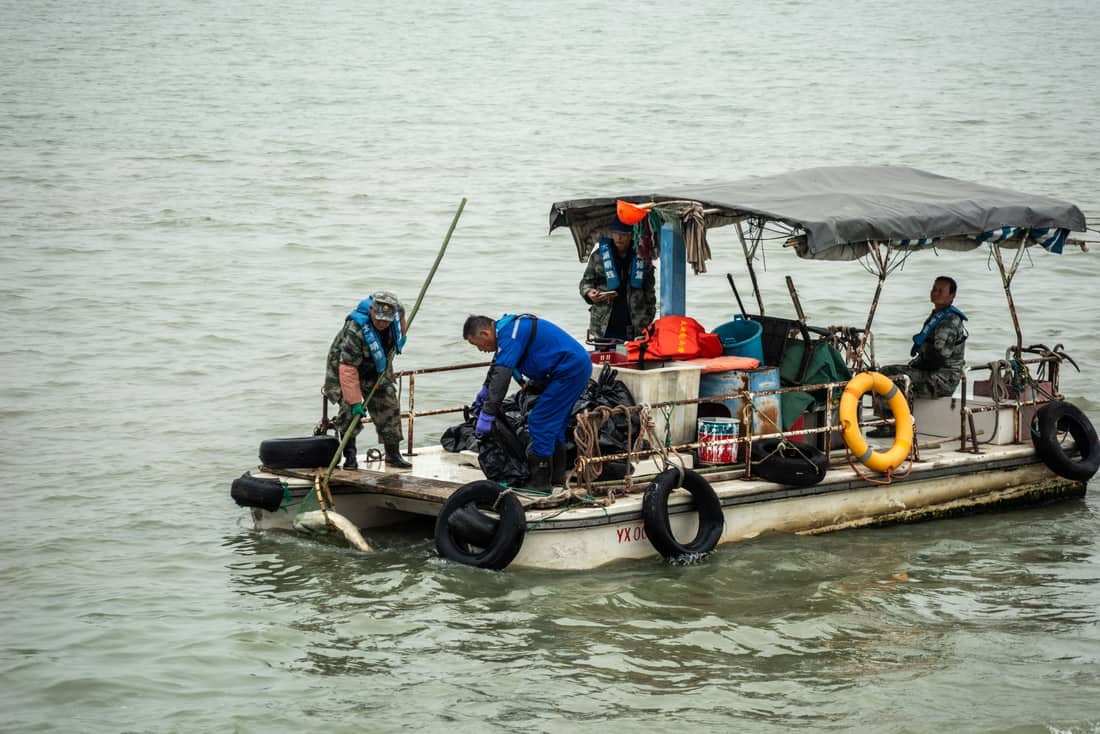 A group of men wearing life vests work on a utility boat on open water, performing maintenance tasks
