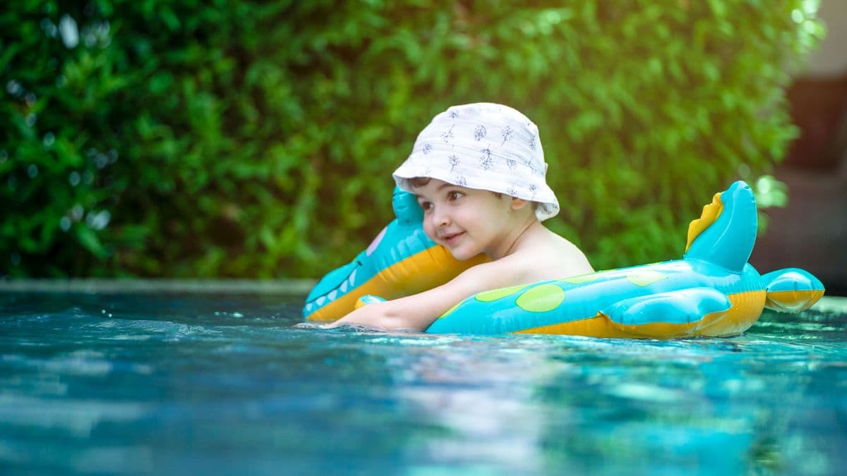 A happy child in a pool wearing a bucket hat and playing with a colorful inflatable toy