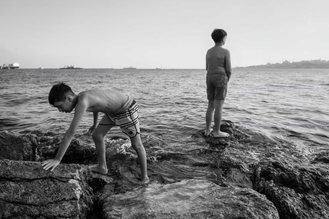 Two boys explore rocks at the seaside, captured in a black and white photograph