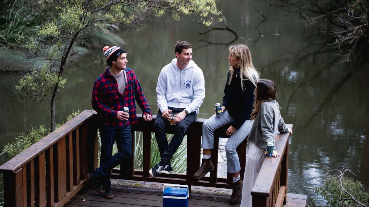 A group of friends enjoying drinks together on a lakeside deck surrounded by nature