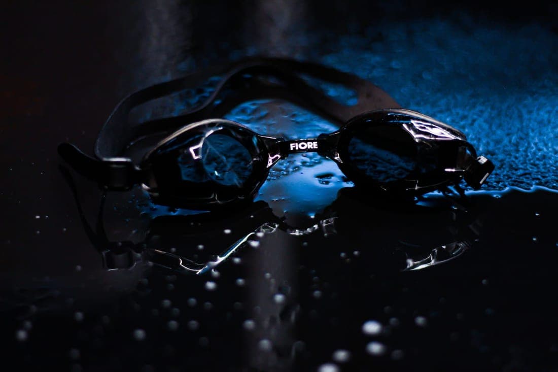 Dark and wet swim goggles on a reflective surface with moody lighting