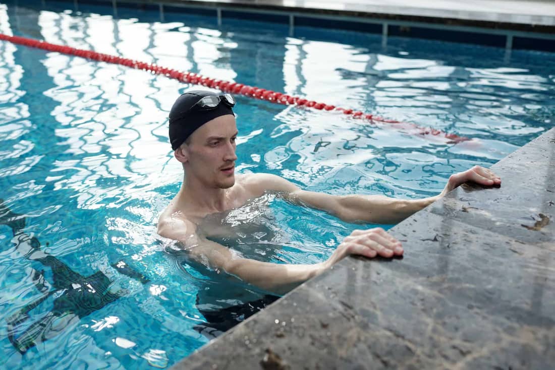 Active young man training in an indoor swimming pool, holding onto a pool edge