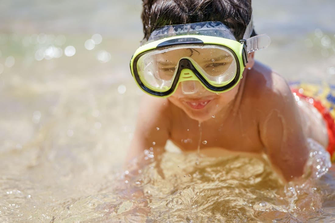 A smiling child wearing goggles enjoys swimming on a sunny summer day
