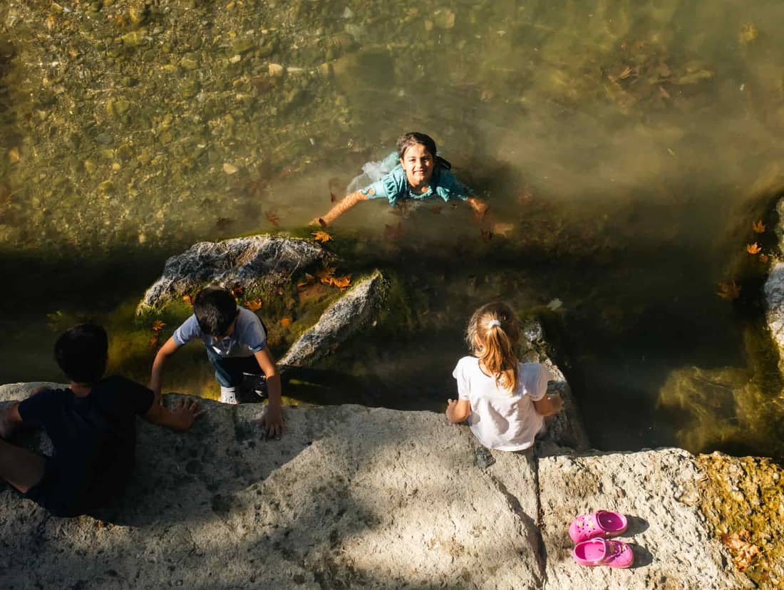 Children enjoying a refreshing swim and playtime by a calm riverbank on a sunny day
