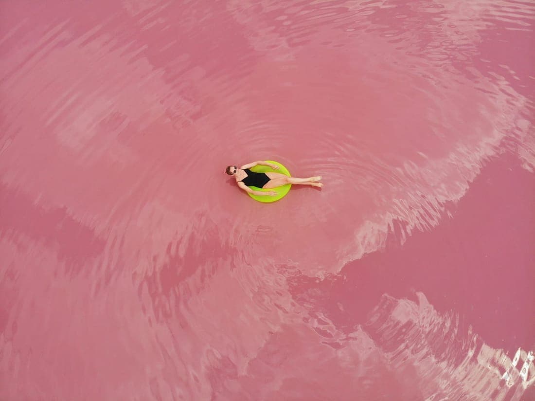 Aerial shot of a woman relaxing on a green float in a vibrant pink lake in Ukraine