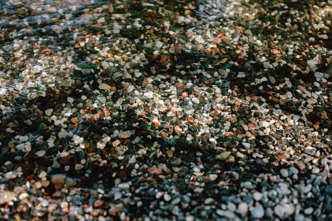 Vibrant pebbles beneath clear water casting intricate reflections in sunlight