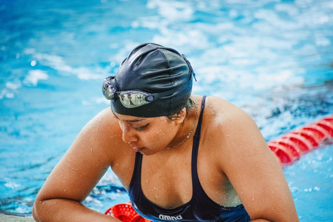 Female swimmer in swim cap and goggles resting poolside, focused and determined