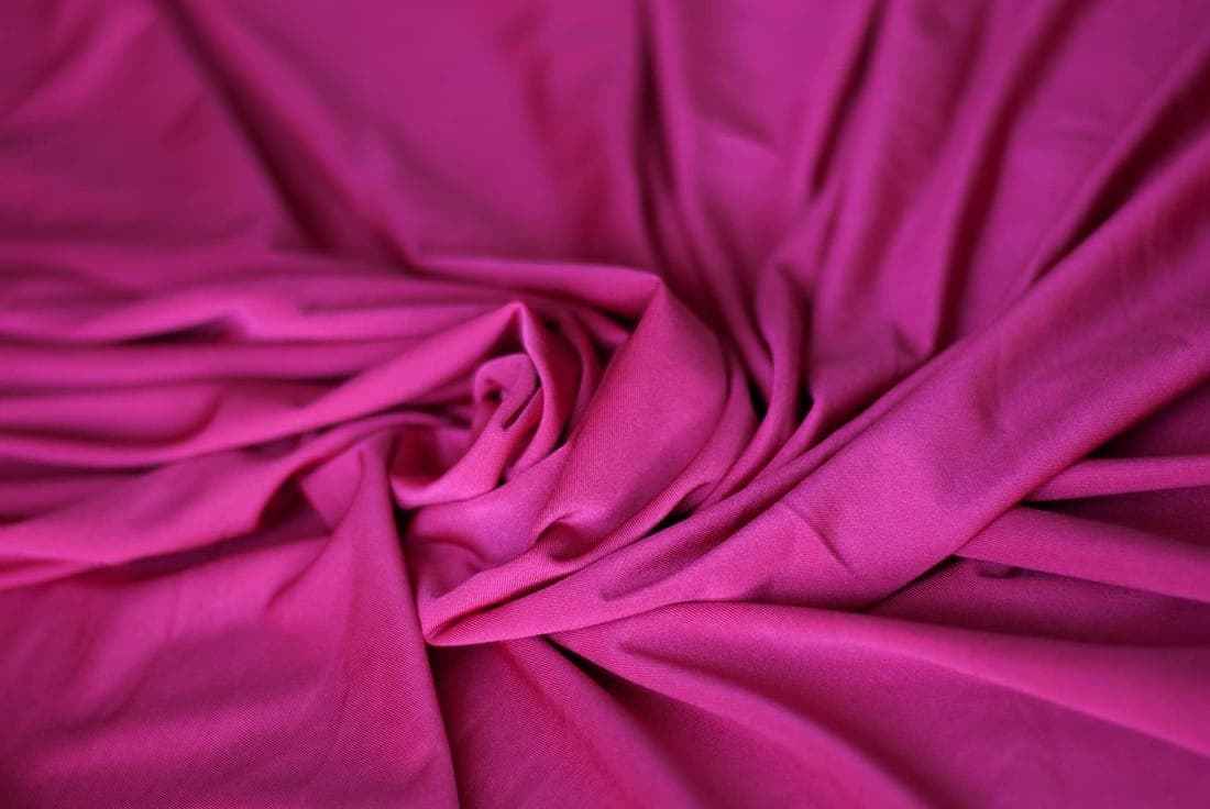 A detailed close-up of vibrant pink fabric with soft wrinkles and a silk-like texture