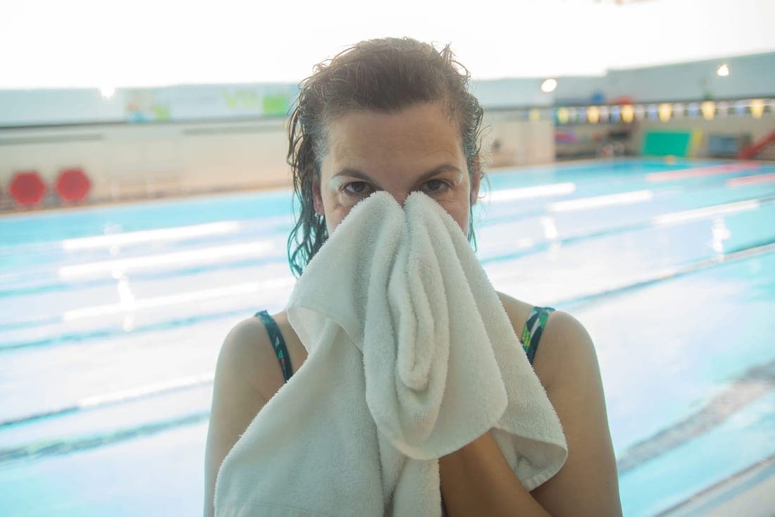 Woman drying her face with a towel at an indoor swimming pool