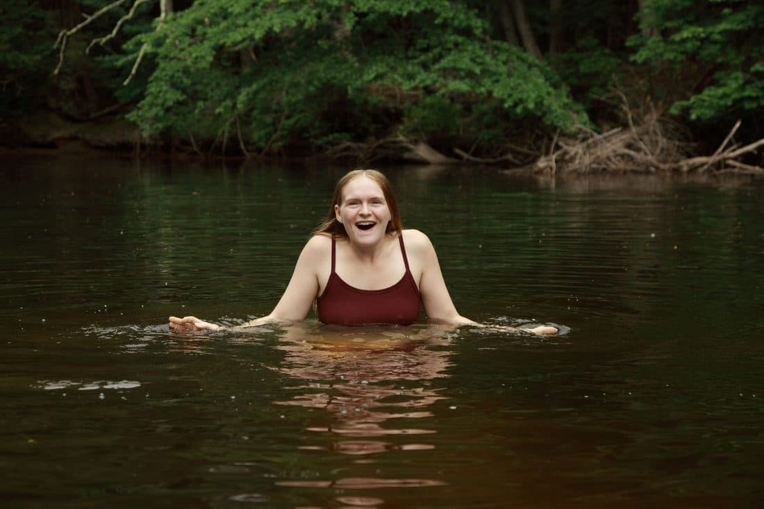 A joyful woman in a red swimsuit swimming in a tranquil lake surrounded by lush greenery