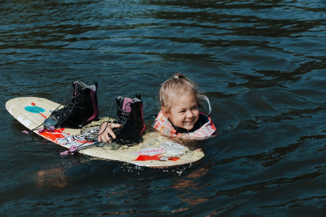 A young girl in a life jacket enjoys wakeboarding on a sunny day in the water