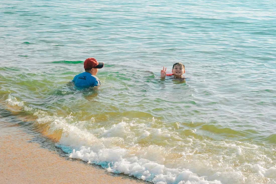 Two boys enjoy playful swimming in the turquoise ocean water by a sandy beach