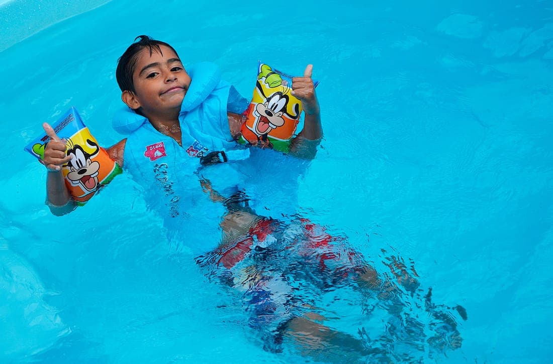 A child playing in the pool, wearing bright floaties and giving thumbs up