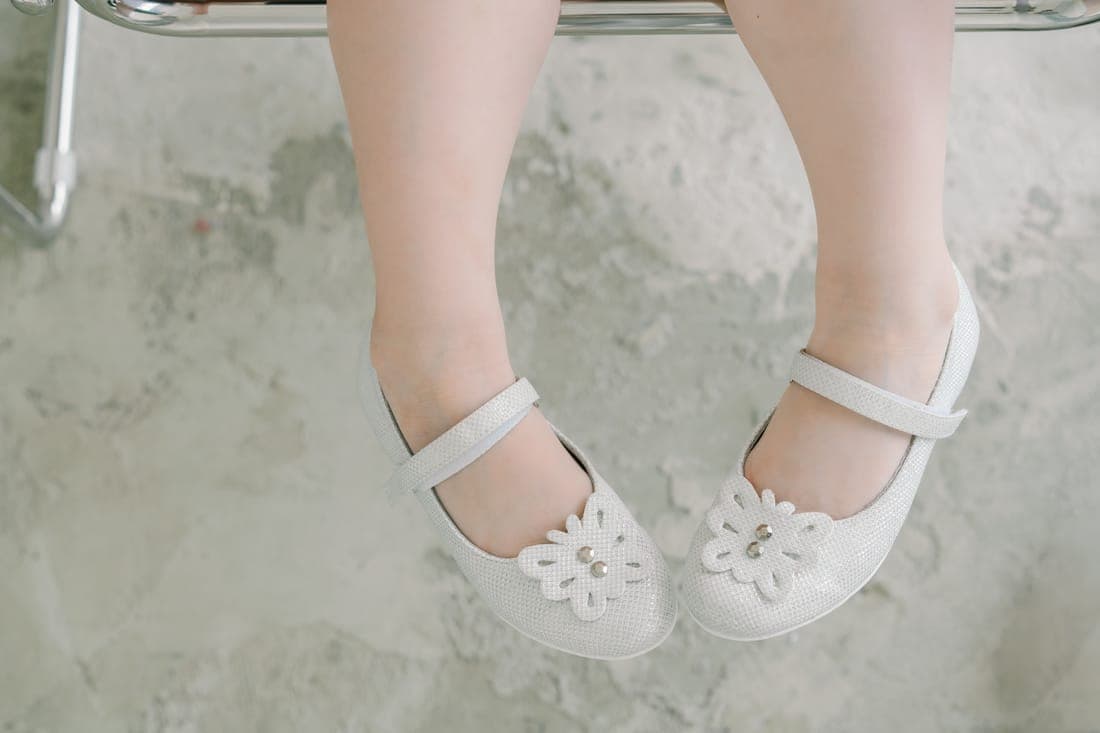 Close-up of child's feet in white doll shoes with floral designs, resting indoors