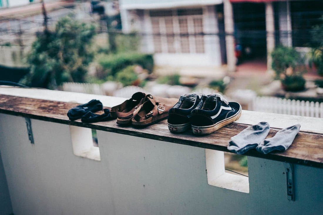 Sandals, sneakers, and socks arranged on a ledge, drying in the outdoor environment