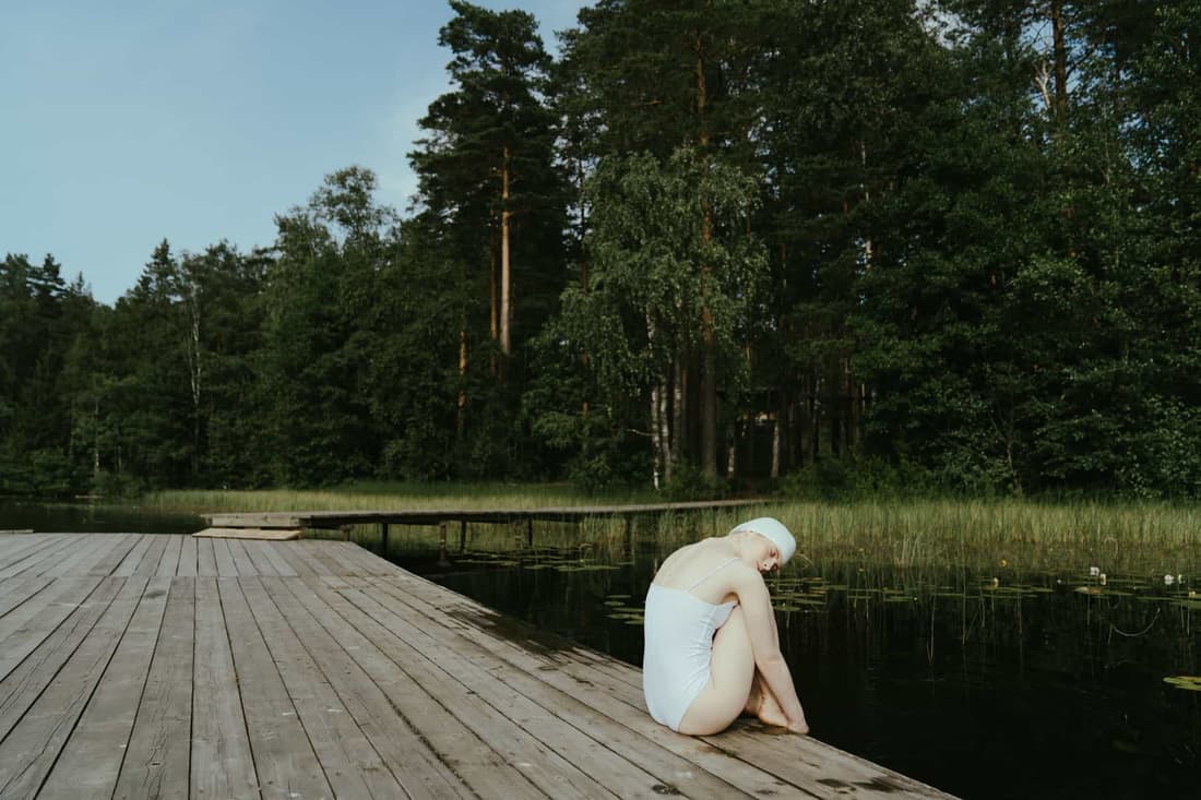 Woman relaxing on a lakeside wooden dock surrounded by lush greenery, embracing tranquility