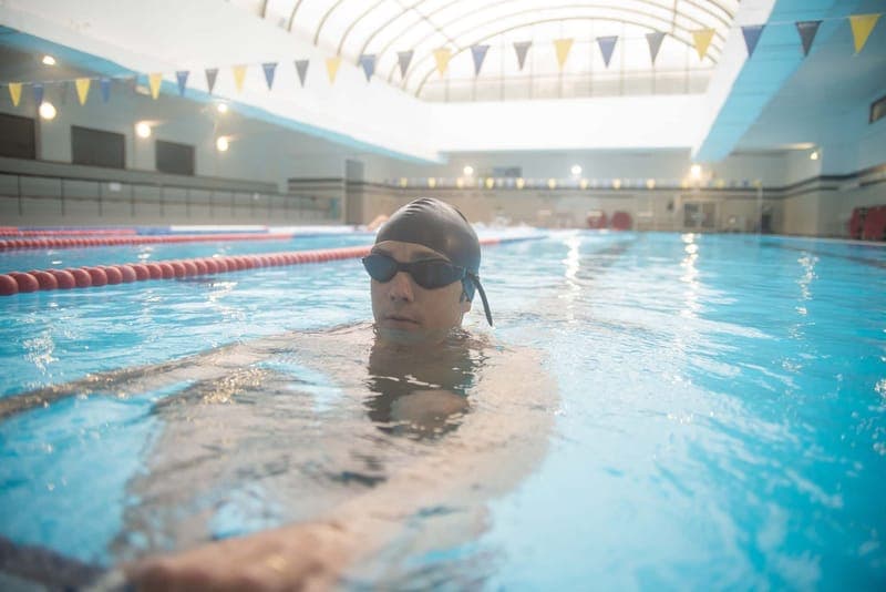 Man swimming in an indoor pool, wearing goggles and cap