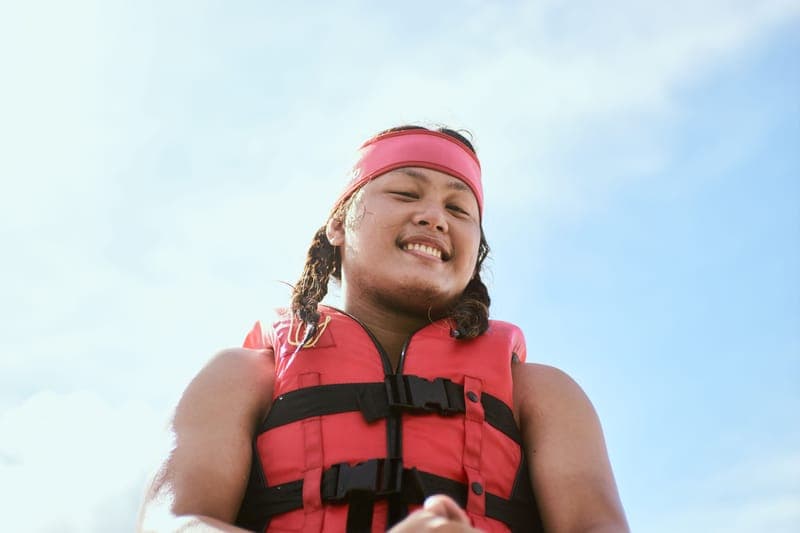 Portrait of a smiling person wearing a red life vest outdoors on a sunny day