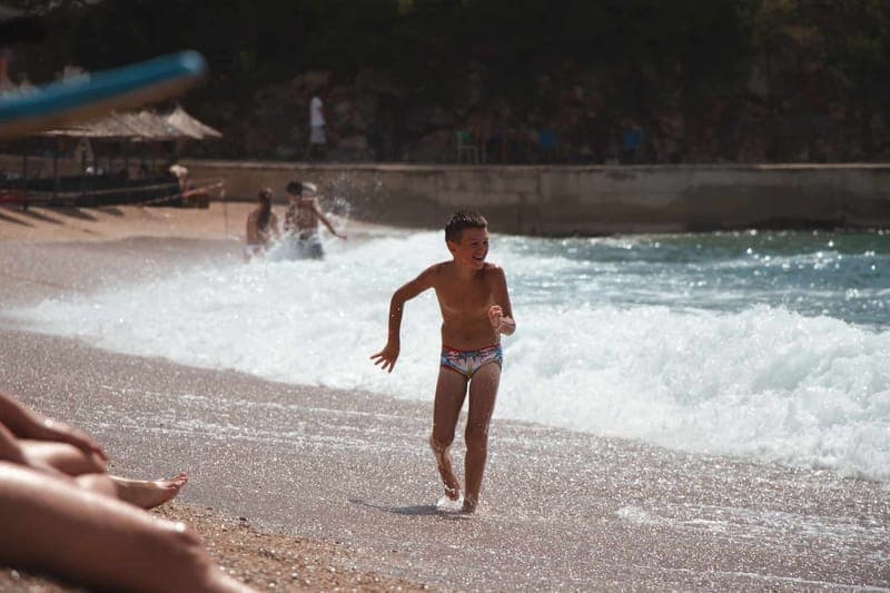 Smiling boy running on summer beach in Vlorë County, enjoying waves and sunshine