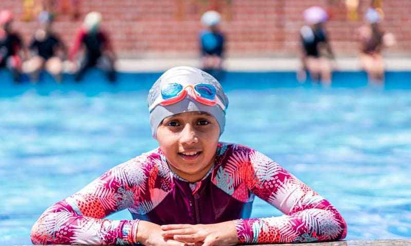 A young swimmer enjoys a sunny day at the outdoor pool, wearing a colorful swimsuit and goggles