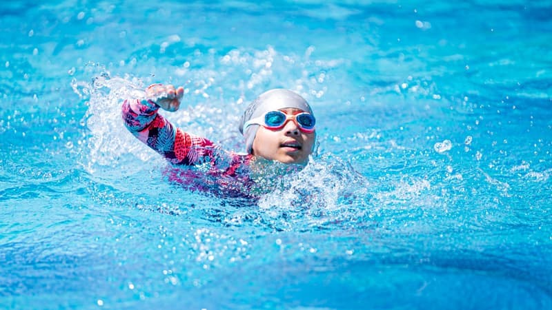 A young swimmer in goggles and cap performing freestyle stroke in a vibrant blue pool