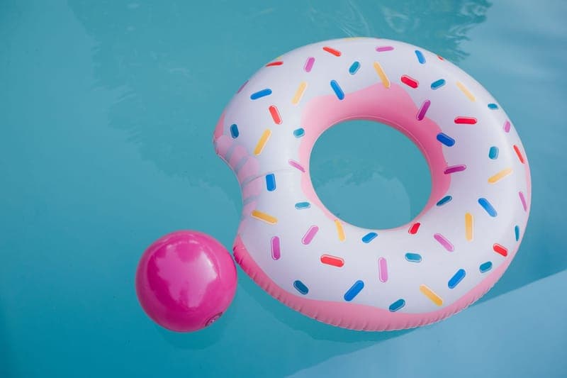 A vibrant donut-shaped inflatable floats beside a pink ball in a clear blue pool