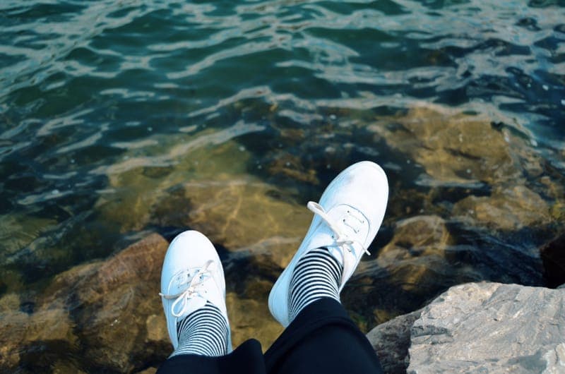 Casual white sneakers paired with striped socks by the water on rocky shore